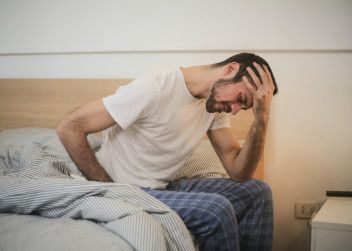 Smutný muž v pyžamu sedící na posteli